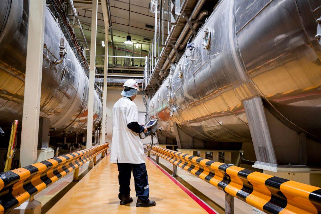 Männlicher Arbeitsinspektionsprozess im Milchpulverkeller mit horizontalen Edelstahltanks