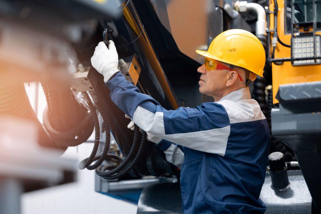 Mechaniker repariert Hydraulikschlauch in Bohrmaschine, Erkundungsbohrung. Erwachsener Mann in Schutzhelm Industriearbeiter.